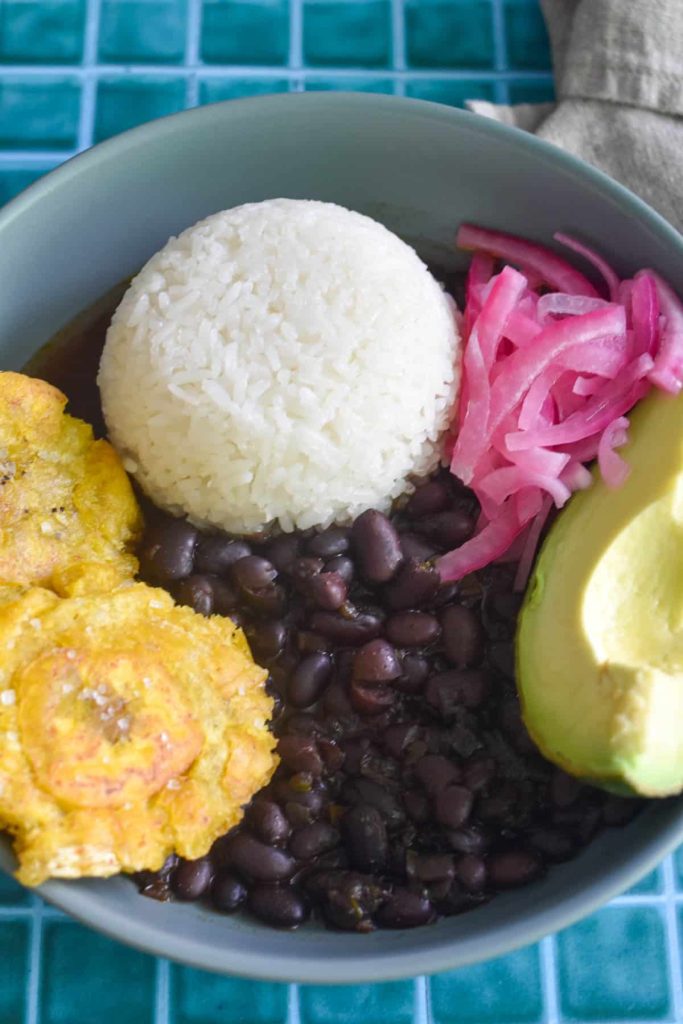 Black beans served next to rice, avocado, plantains and onions. 