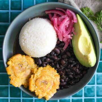 Menestra with rice, avocado, plantain and onion in a light blue bowl.