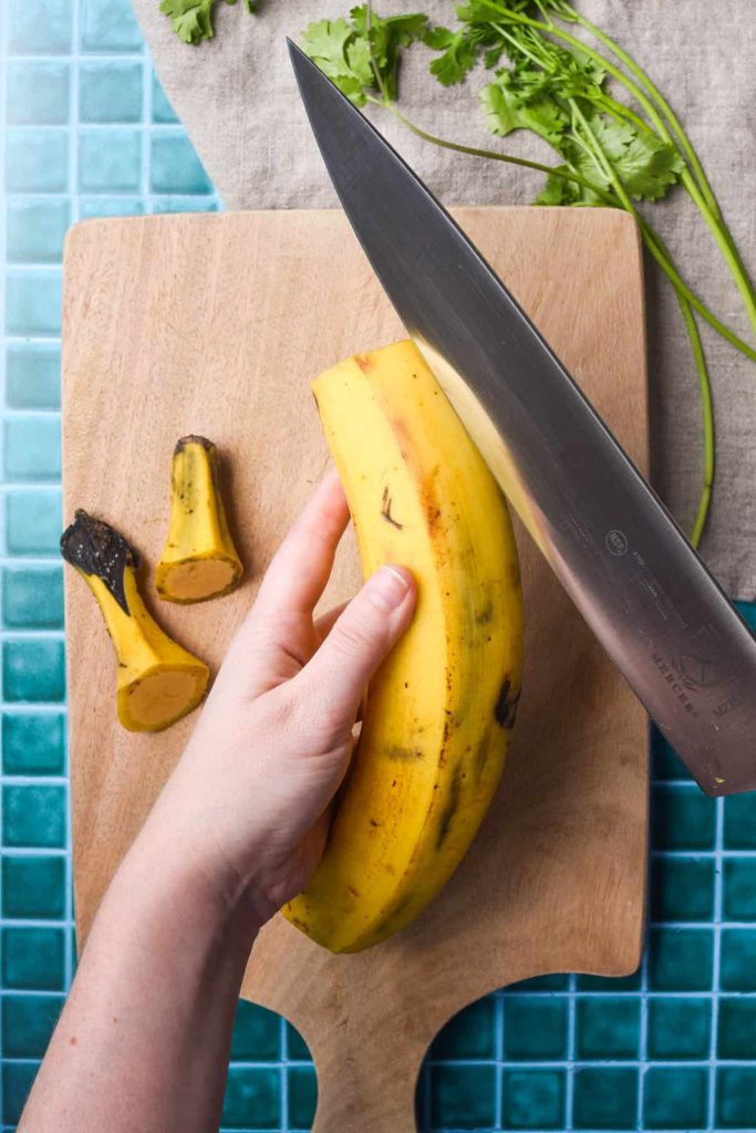 Hand holding a plantain and knife to take the peel off. 