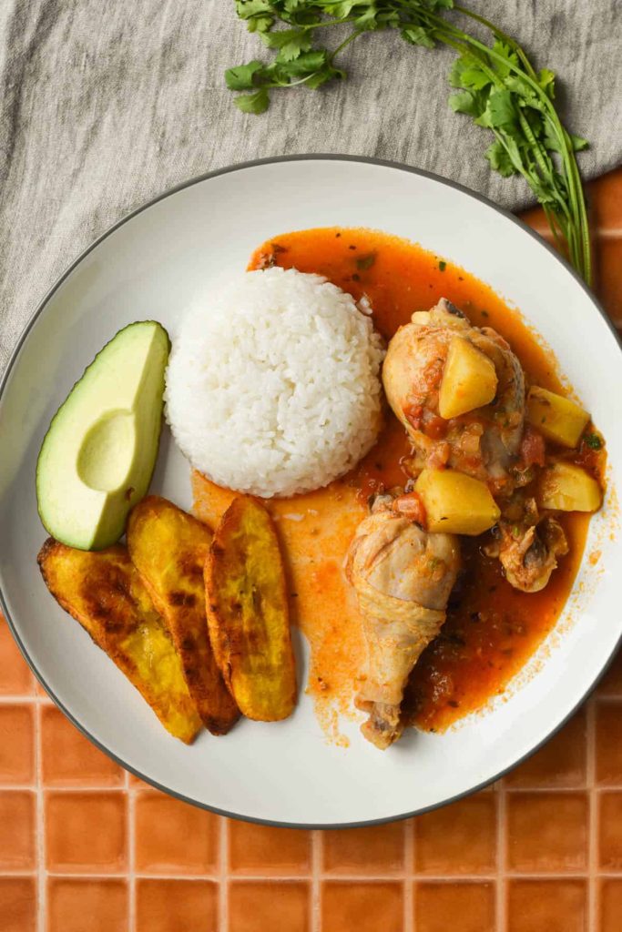 Maduritos served with stewed chicken, rice and avocado on a plate. 