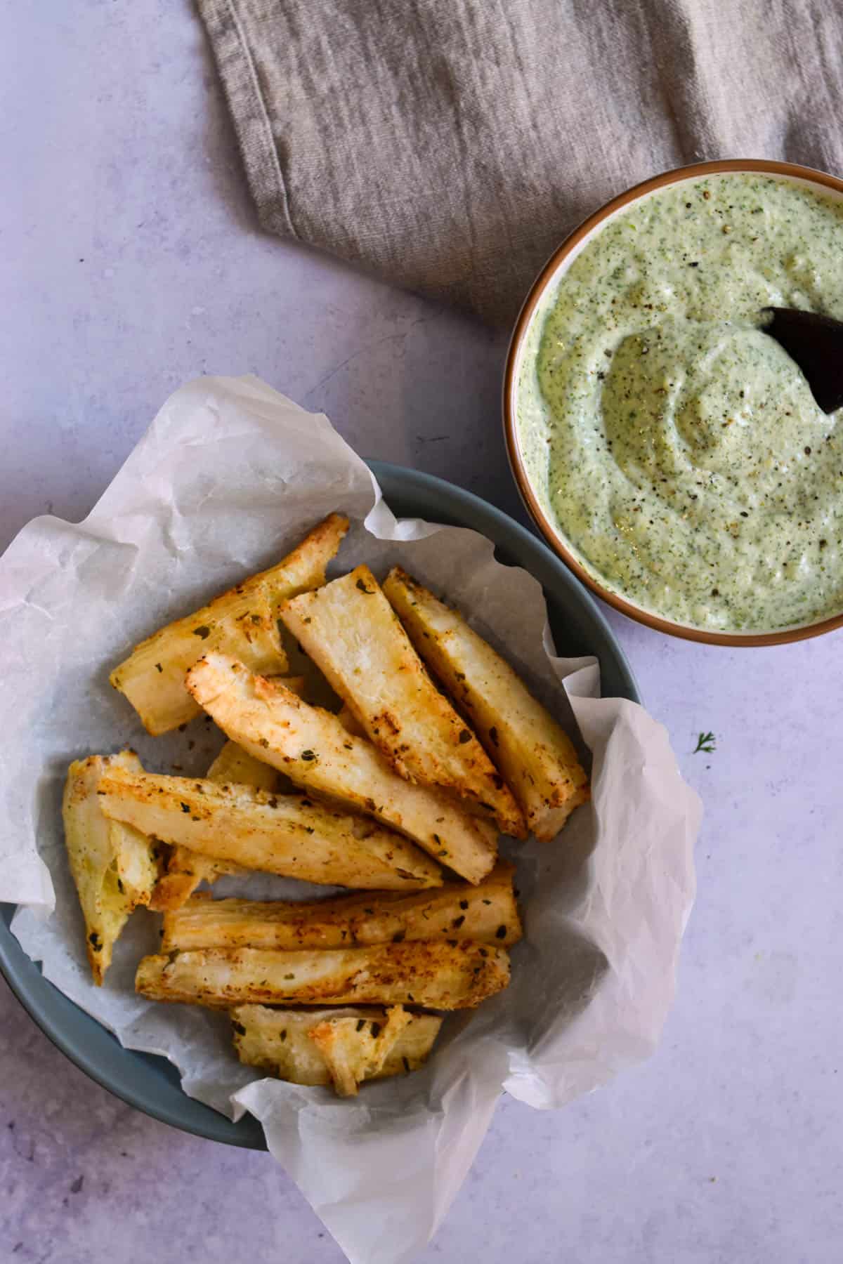 Overhead shot of yuca fries in a plate next to a bowl of green sauce. 