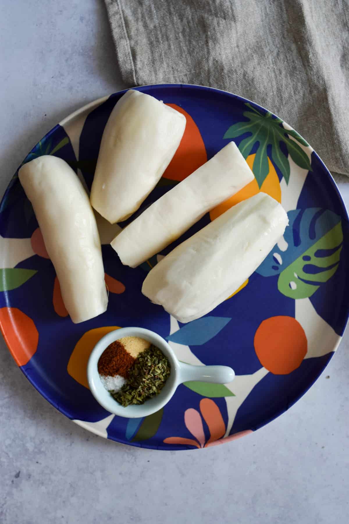 Freshly peeled yuca on a plate next to a small bowl of seasonings. 