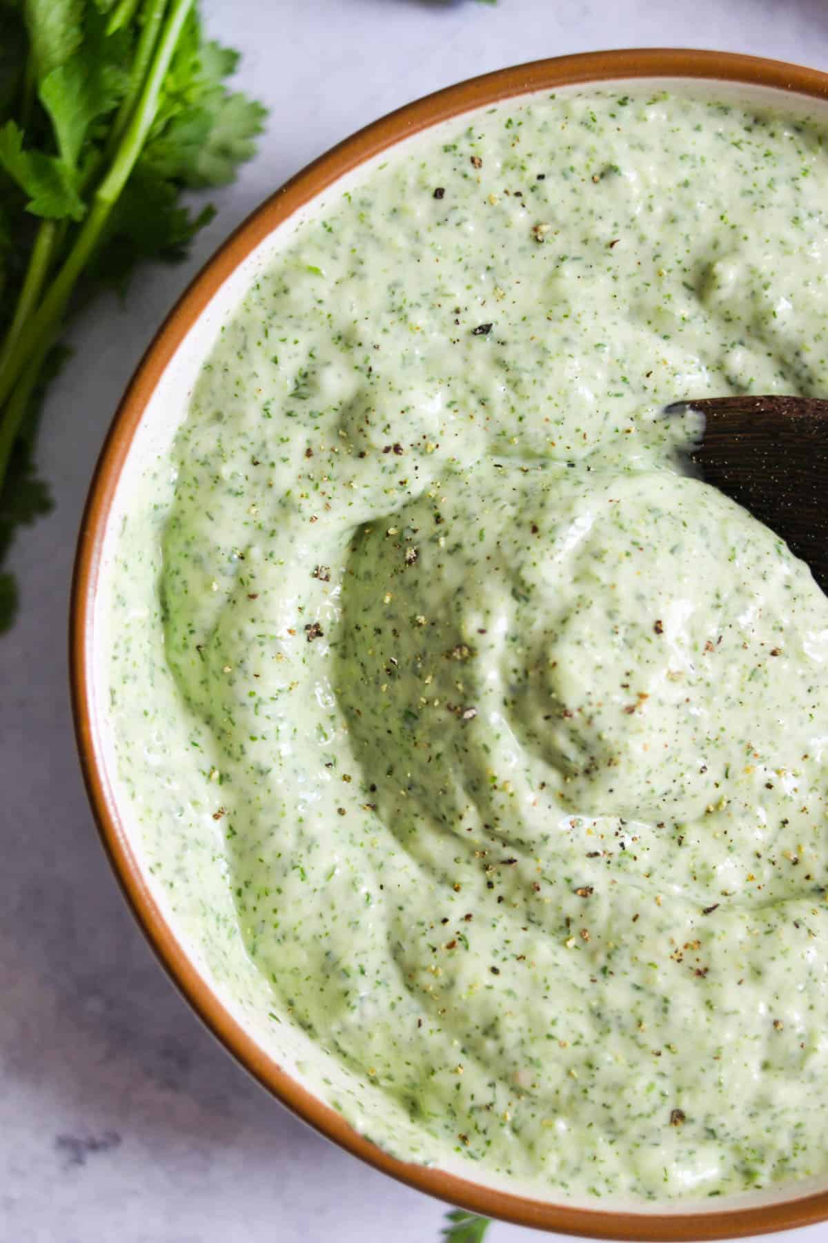 Close up shot of cilantro jalapeno sauce in a bowl with a wooden spoon. 