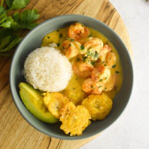 Overhead shot of camarones al ajillo in a bowl with rice, plantains and avocado on the side.