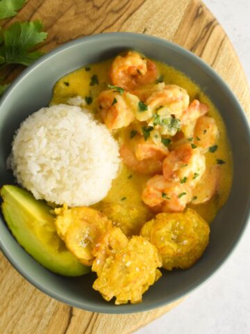 Overhead shot of camarones al ajillo in a bowl with rice, plantains and avocado on the side.