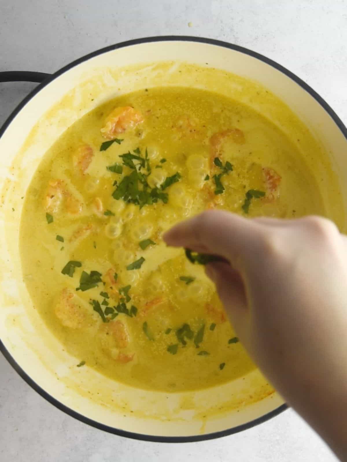 Sprinkling fresh parsley over the camarones al ajillo in a skillet.