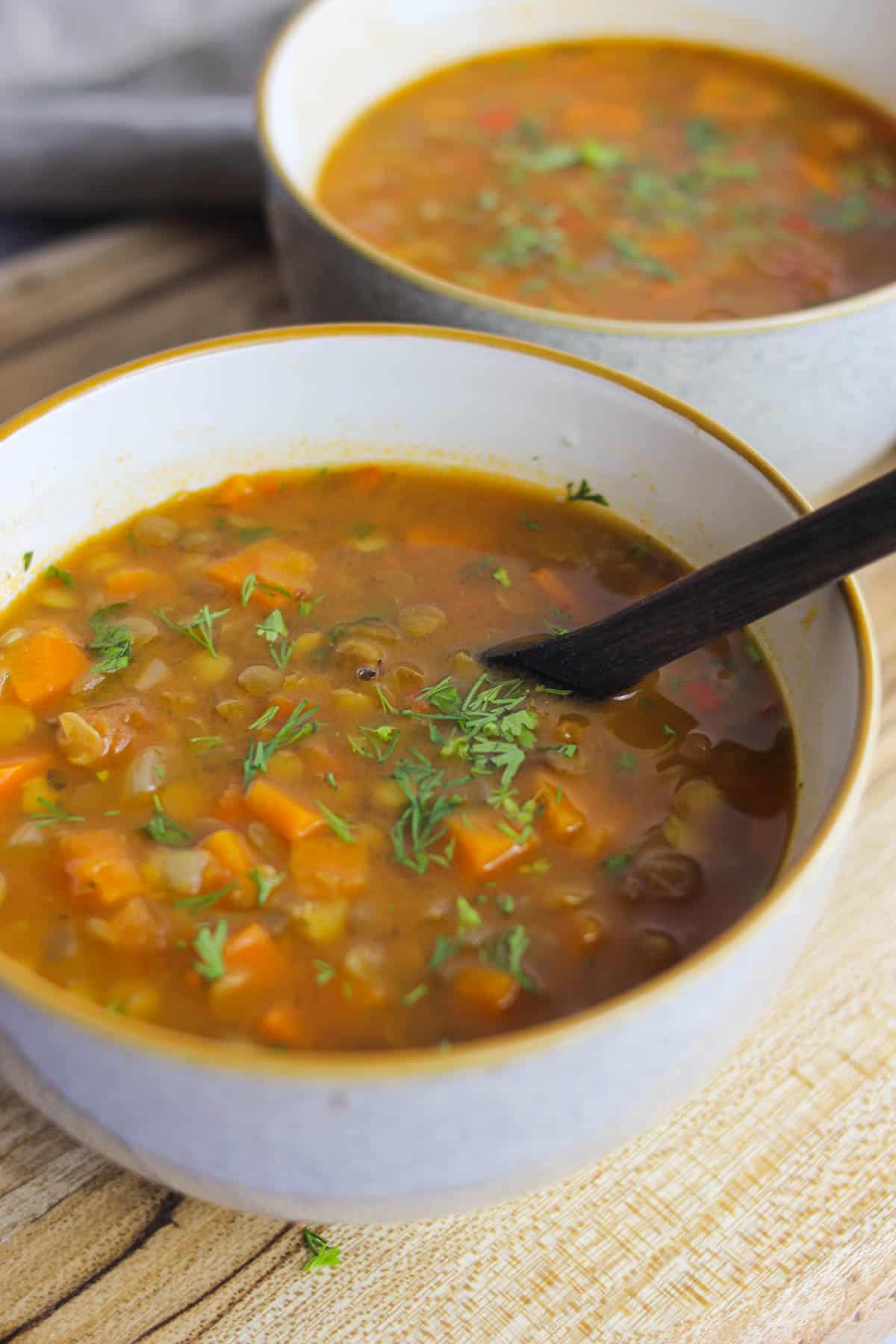 Two bowls of carrot and lentil soup on a wooden background.