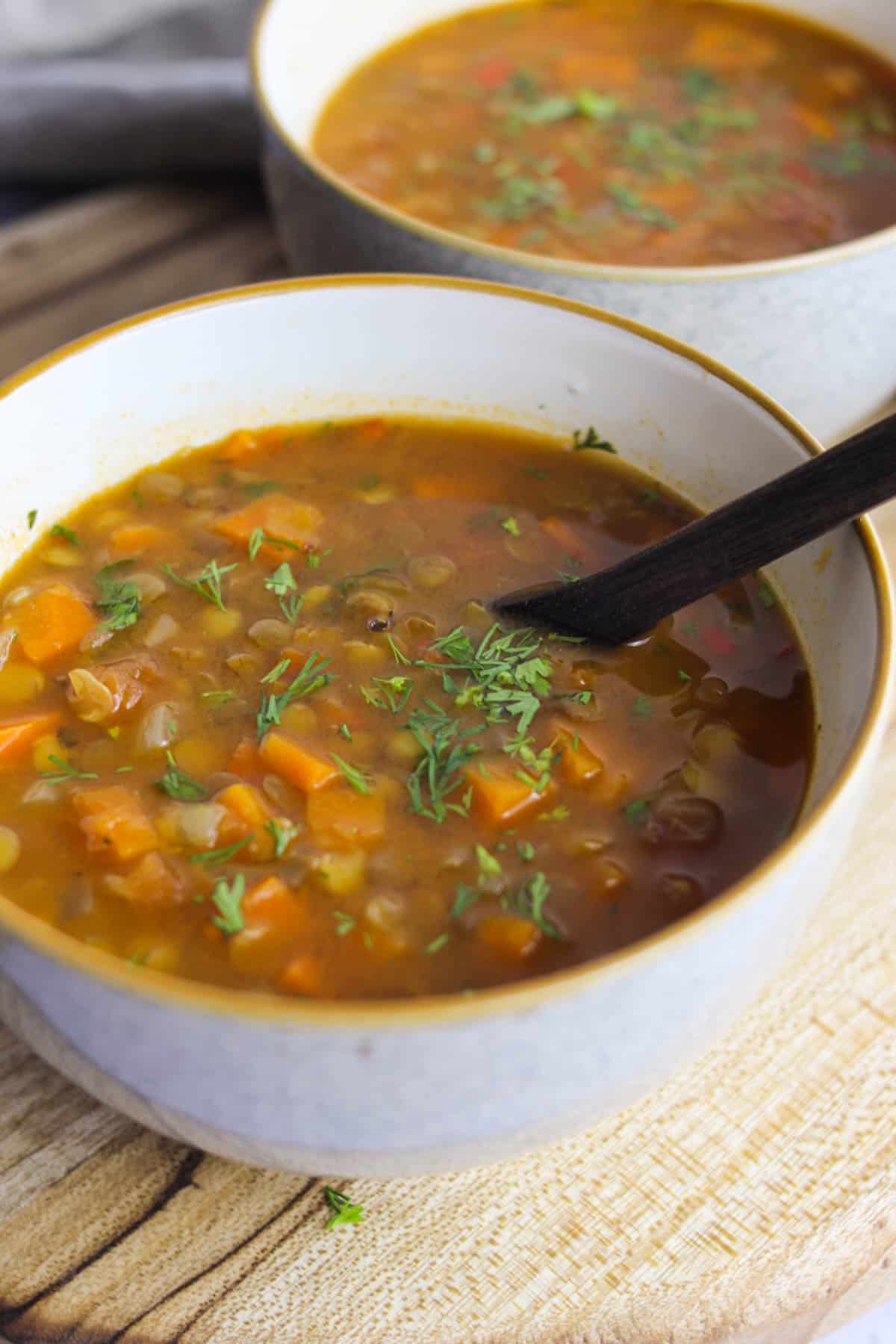 Two bowls of carrot and lentil soup lined up on a wooden board.