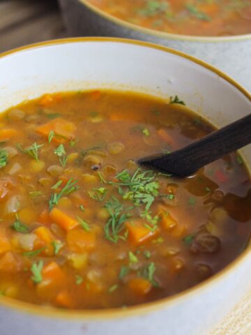 Carrot and lentil soup served in a white bowl with cilantro sprinkled on top.